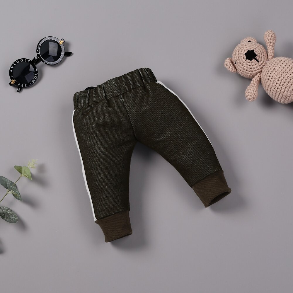 Baby pants with white side stripes, a pink crocheted bear, black sunglasses, and green leaves are arranged on a grey surface, perfect accessories for a reborn baby girl.