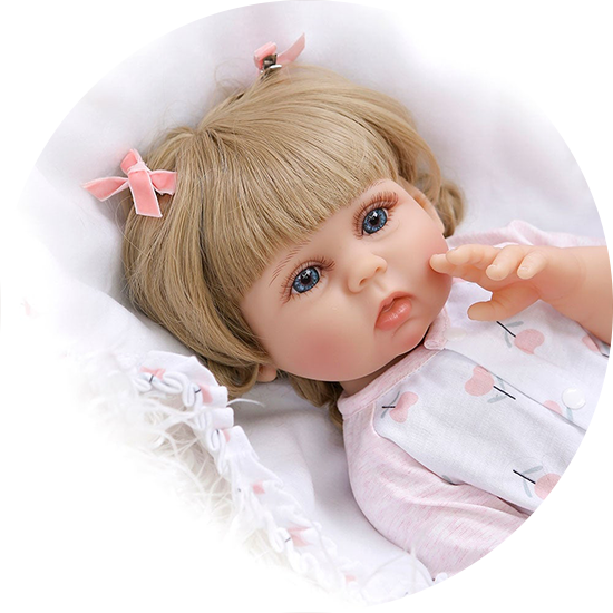 A lifelike baby doll with blonde hair and blue eyes, wearing a white and pink outfit, lying on a soft, white blanket.