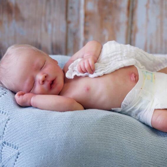 Newborn baby sleeping peacefully on a light blue blanket, with a white cloth partially covering them.