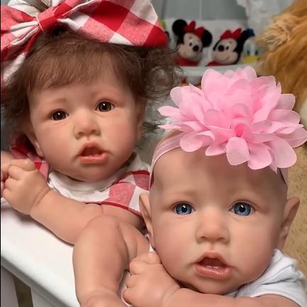 Two lifelike reborn baby girls with large bows on their heads, one in red and white, the other in pink, placed on a white surface. Perfect for any doll supplier seeking detailed and realistic baby dolls.